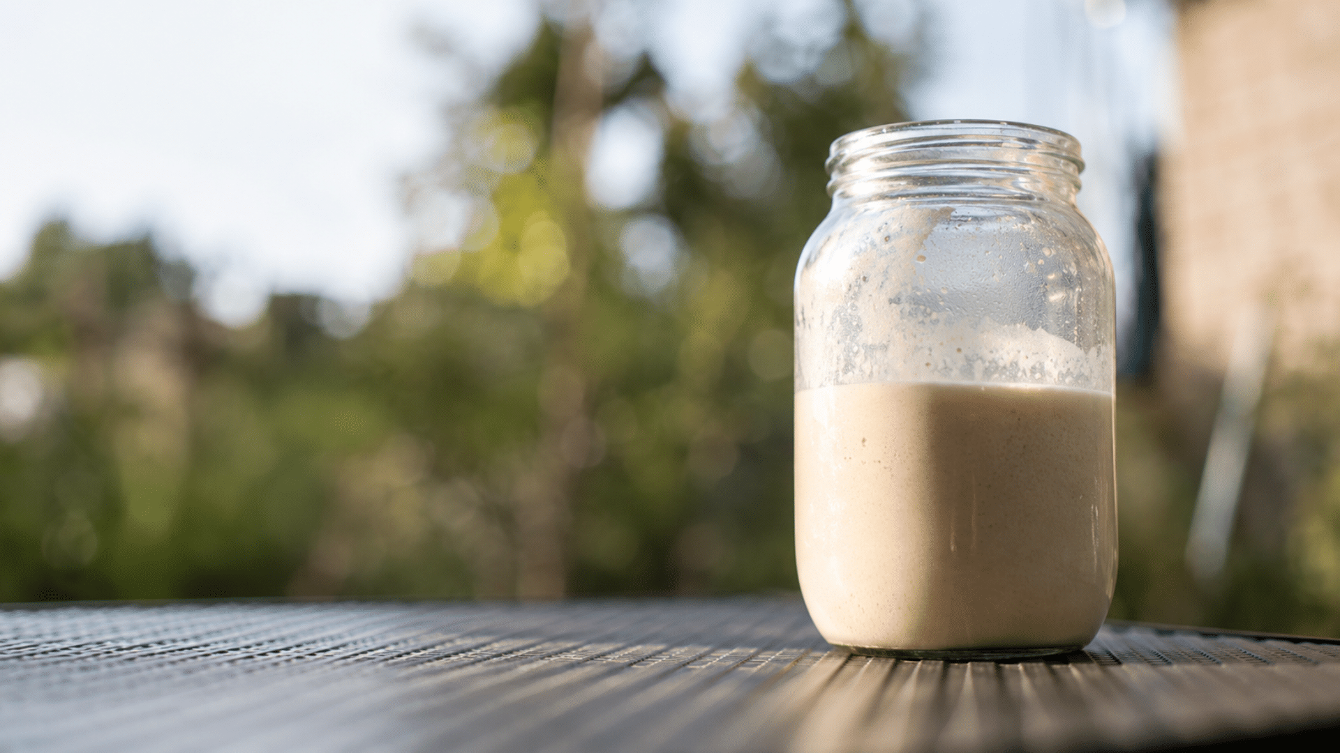 Glass jar of raw milk sitting on an outdoor table.