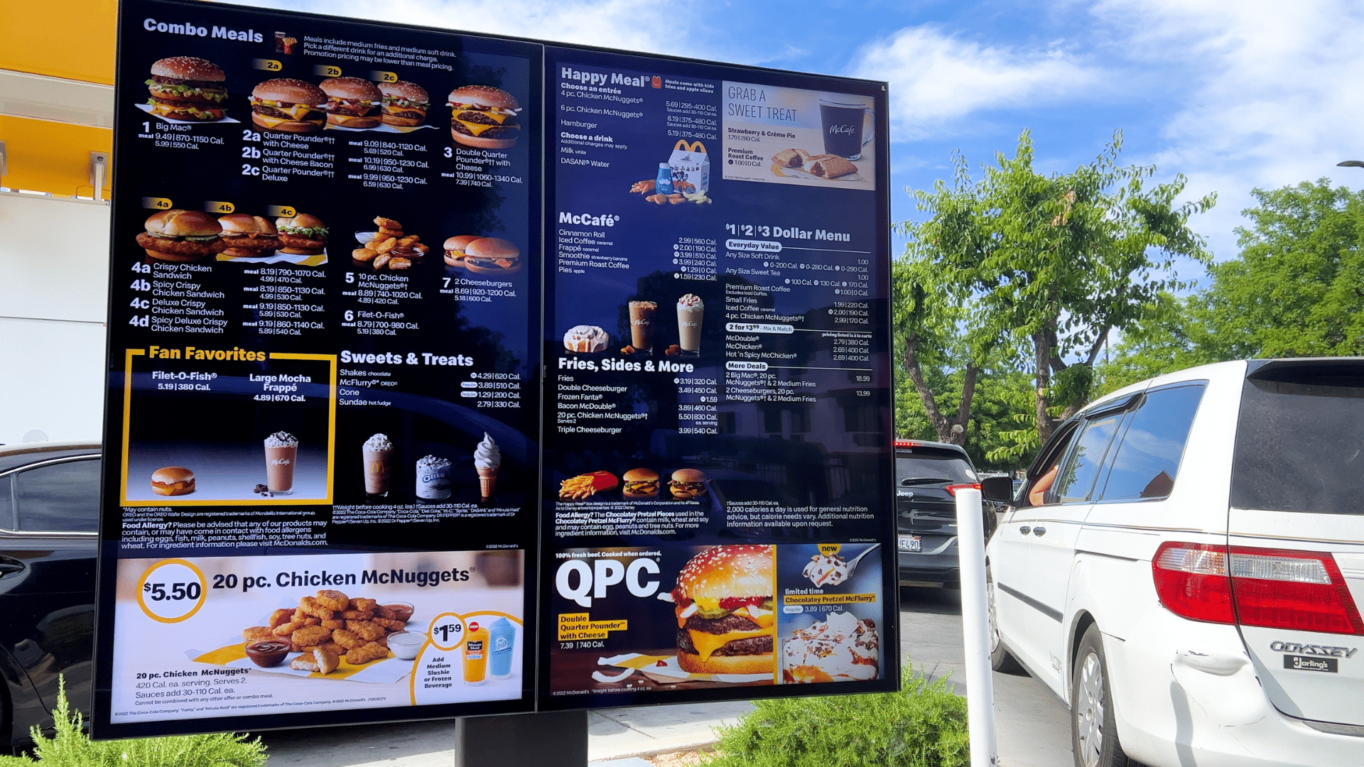 A digital McDonald's drive-thru menu board displaying various meals and prices next to a white minivan.