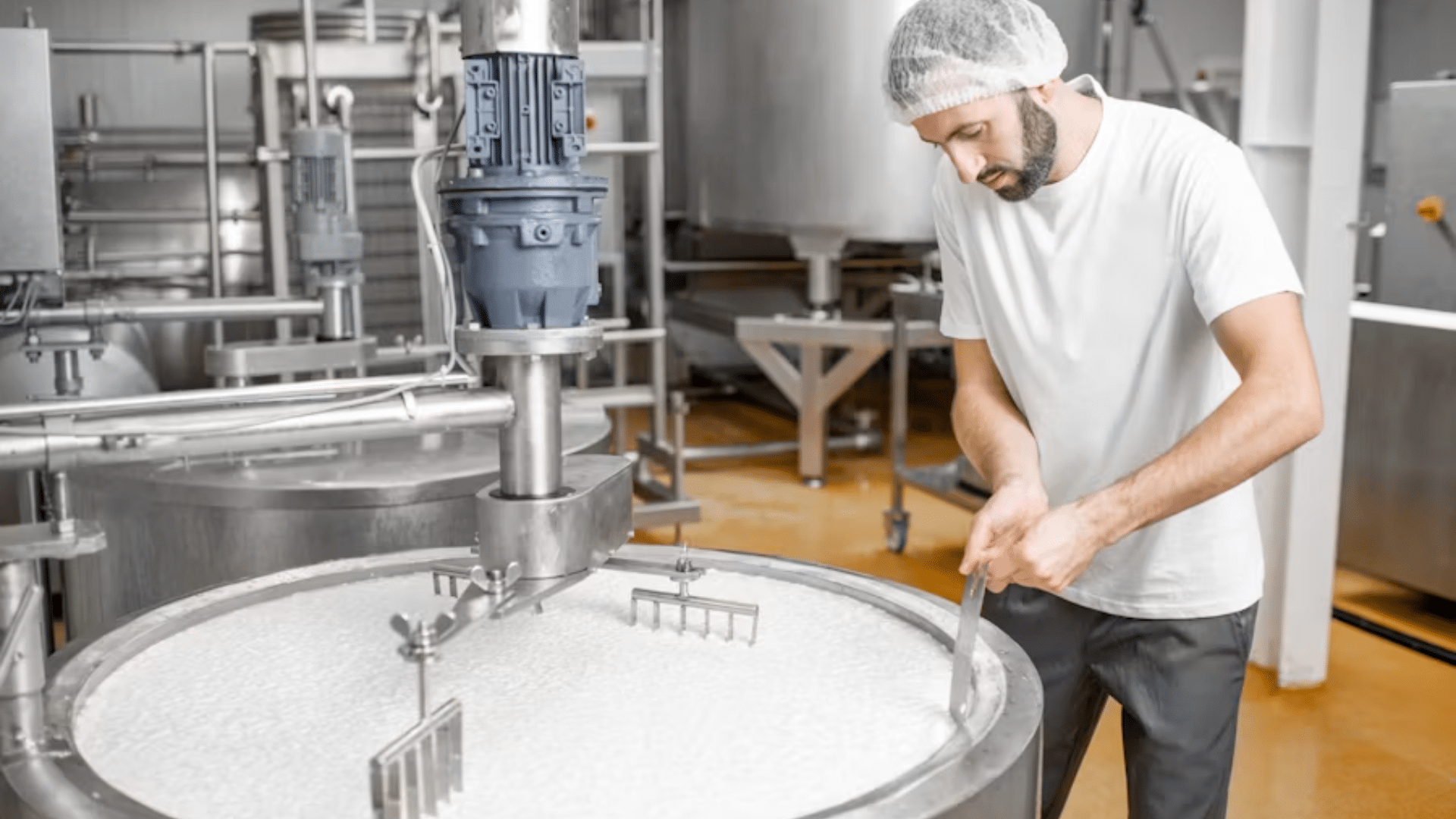 Worker stirring liquid in a large stainless steel food production tank.