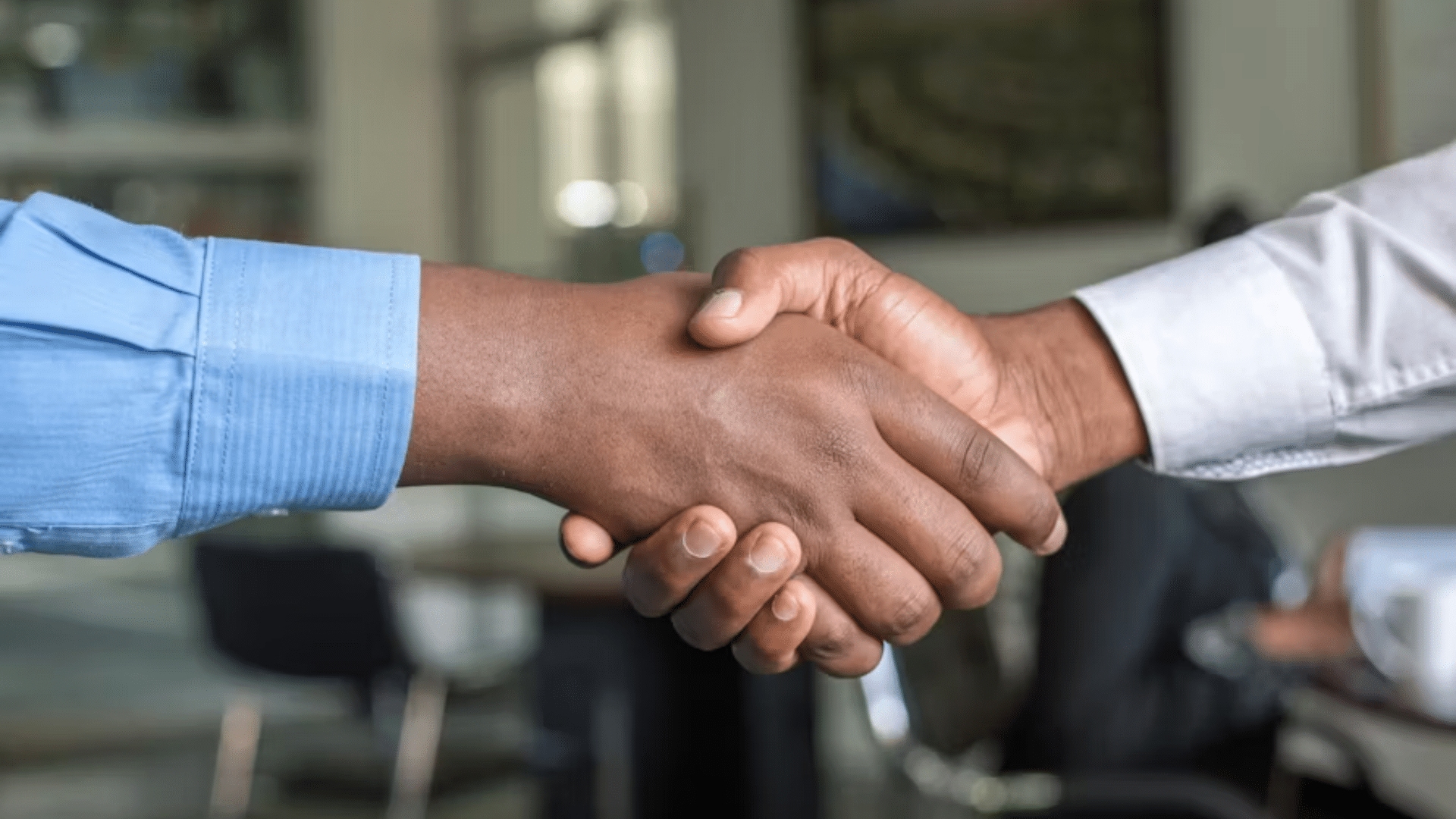 Two business professionals shaking hands in an office setting to finalize an agreement or partnership.
