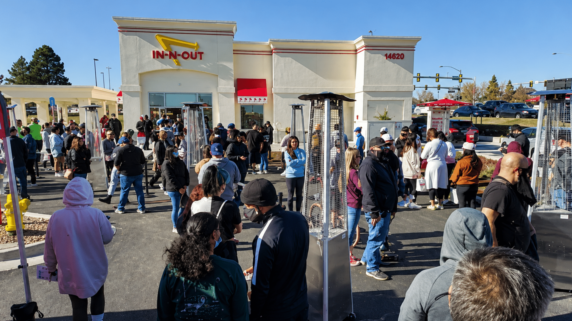 A large crowd of people waiting in outdoor lines under a clear sky in front of an In-N-Out Burger restaurant.