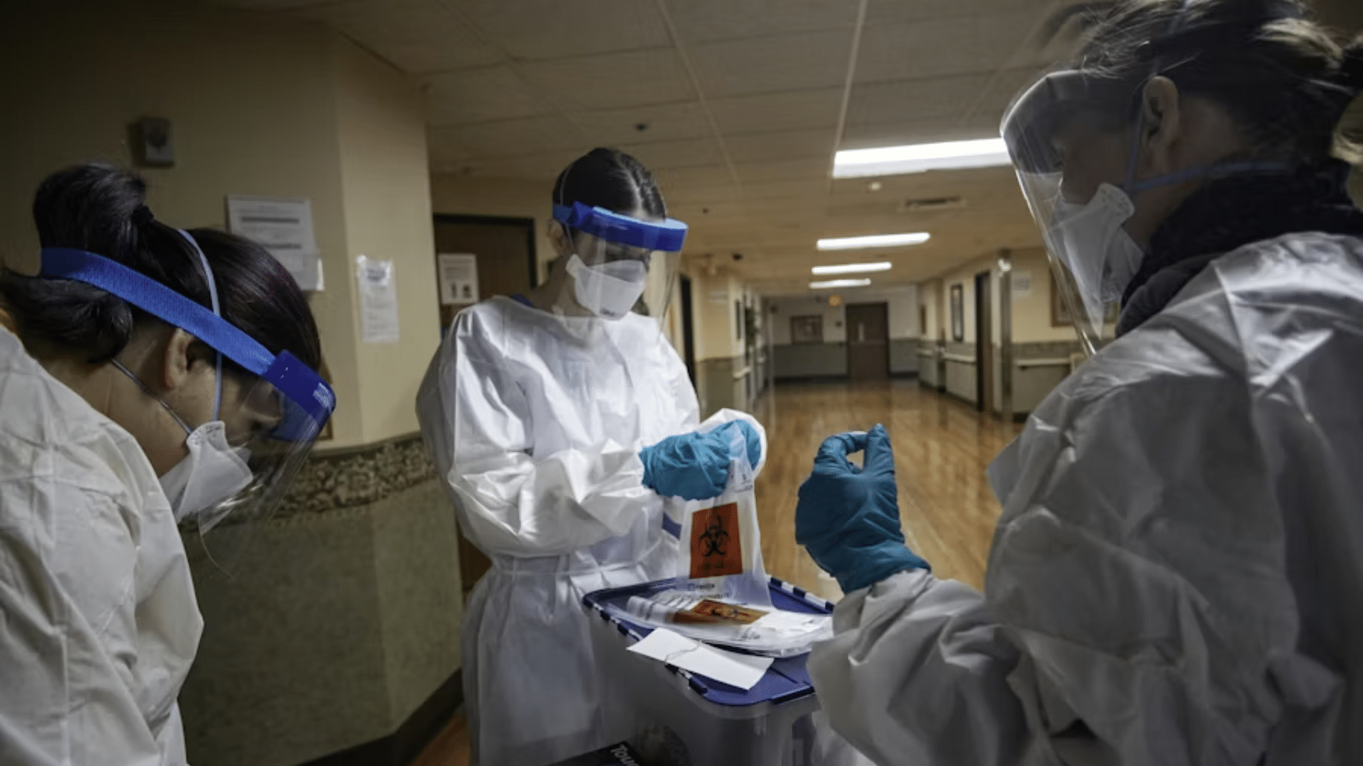 Health care workers in protective gear handling biohazard sample bags.