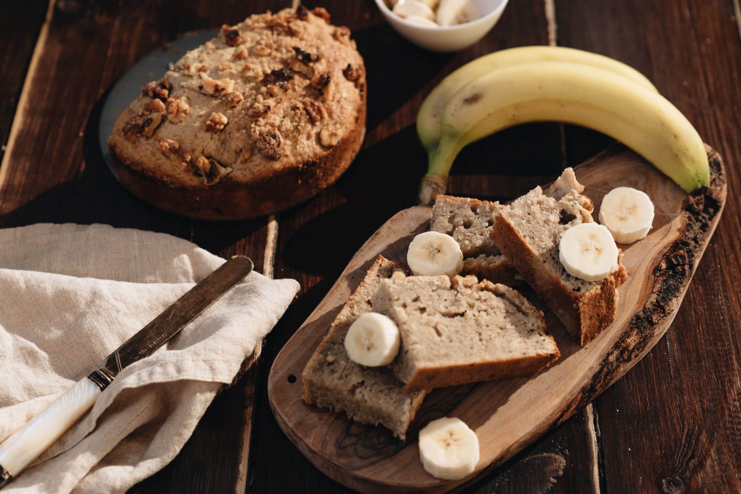 Slices of homemade banana bread served with fresh banana slices on a wooden board.
