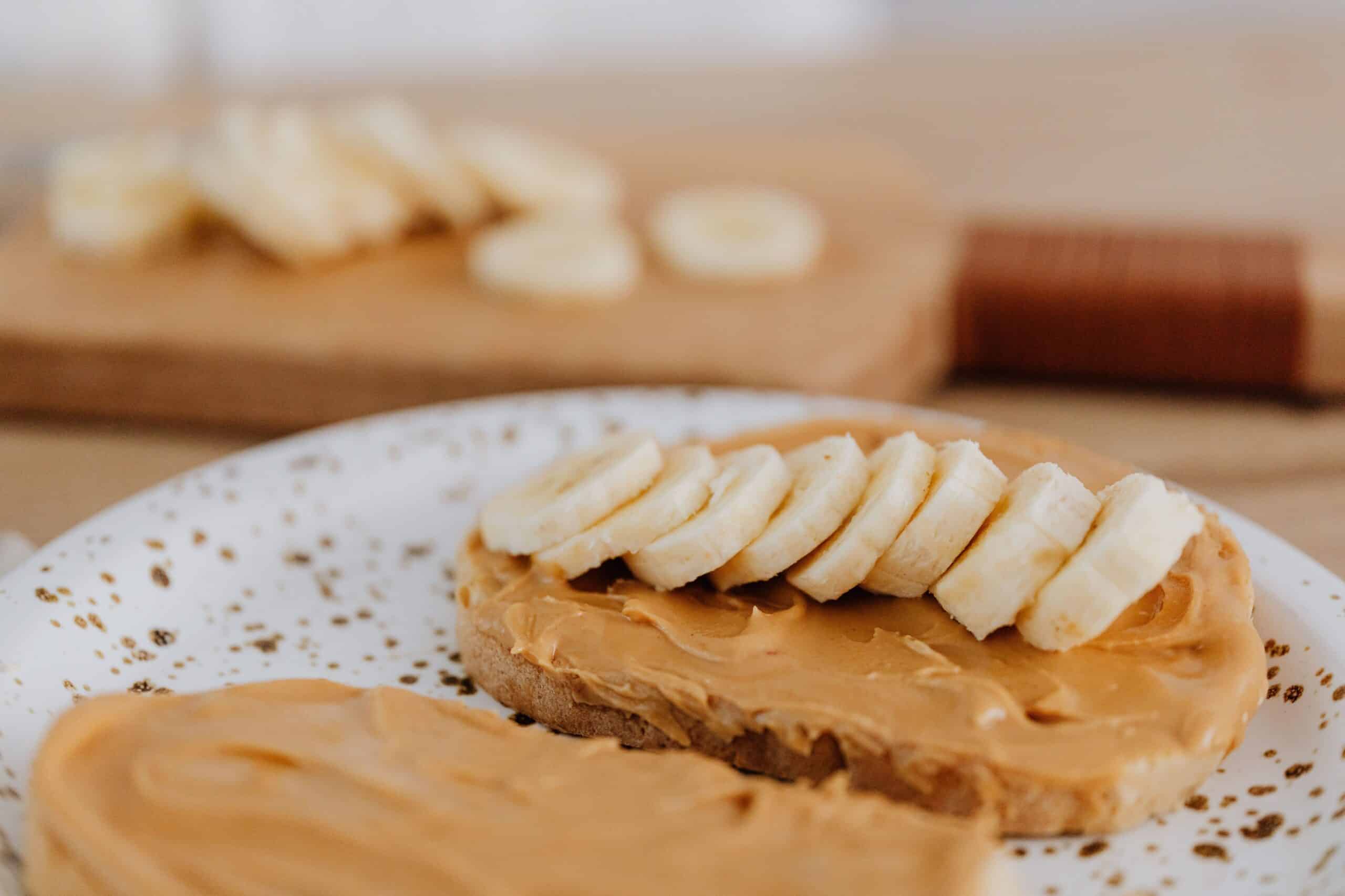 Peanut butter toast topped with sliced banana on a plate.