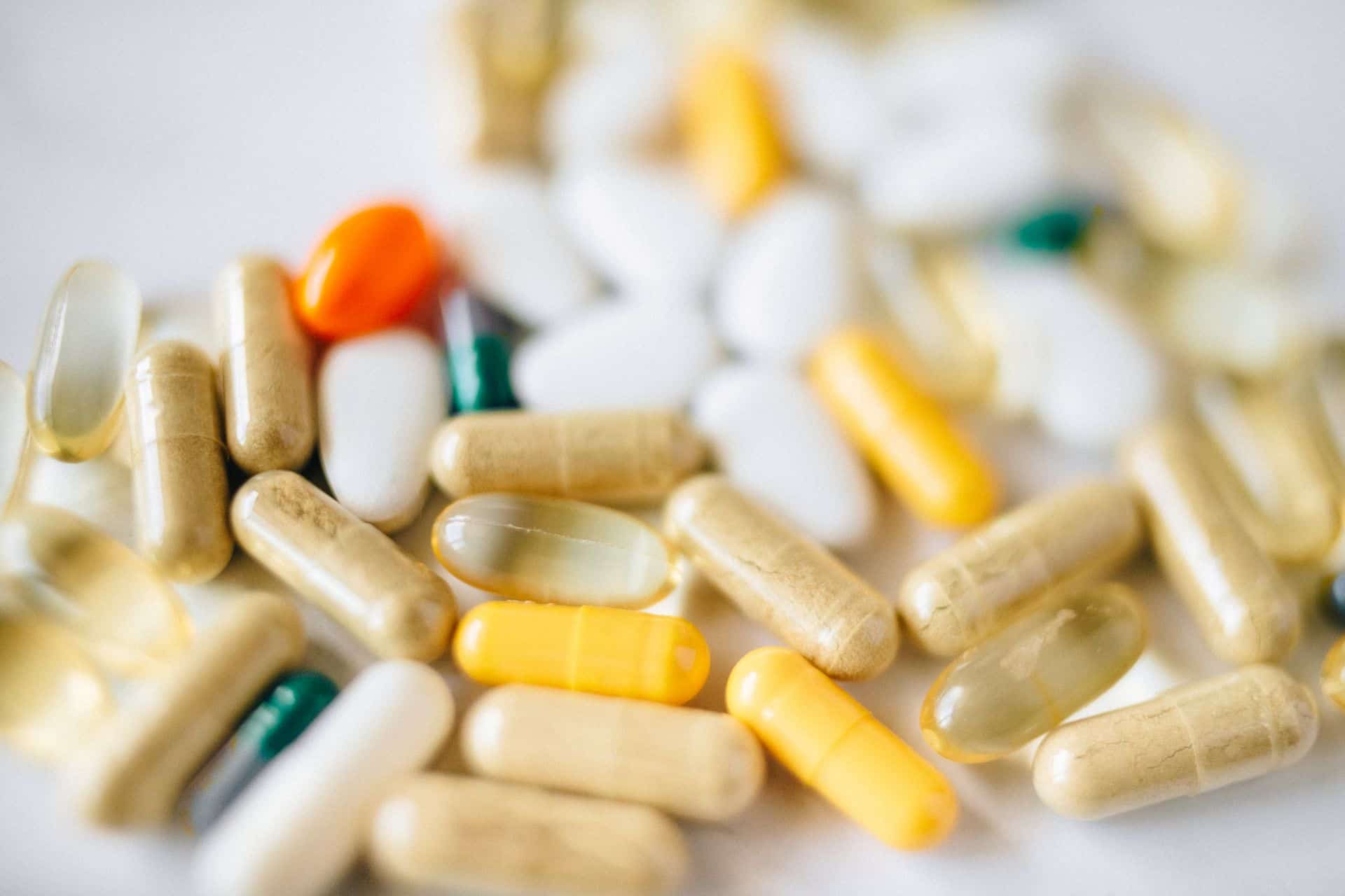 Assorted medicinal capsules, softgels, and tablets scattered across a white surface.