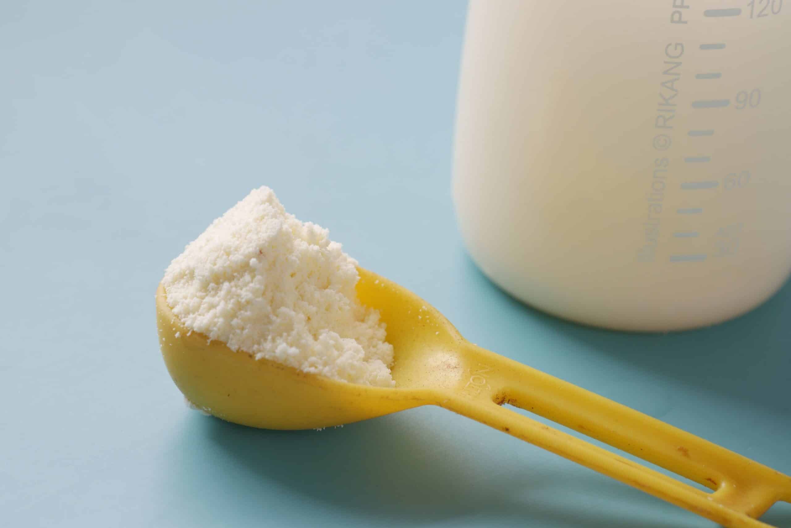 Powdered milk in a yellow measuring scoop beside a bottle.