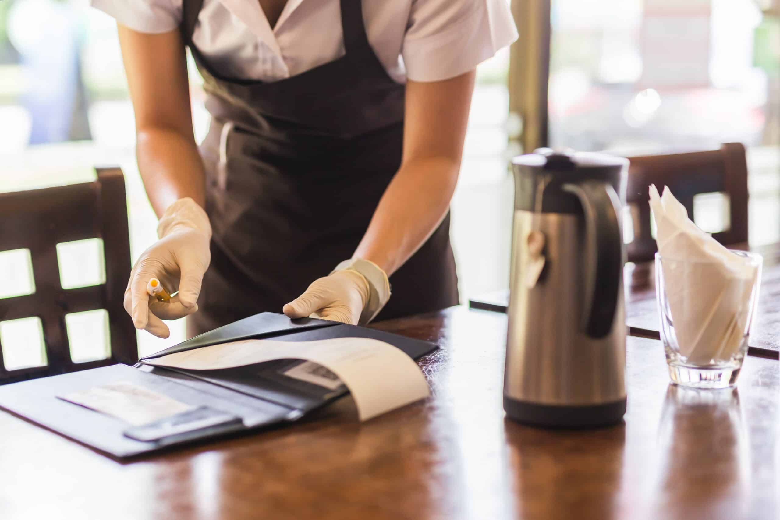 Restaurant employee reviewing paperwork or a bill folder at a dining table while wearing disposable gloves.