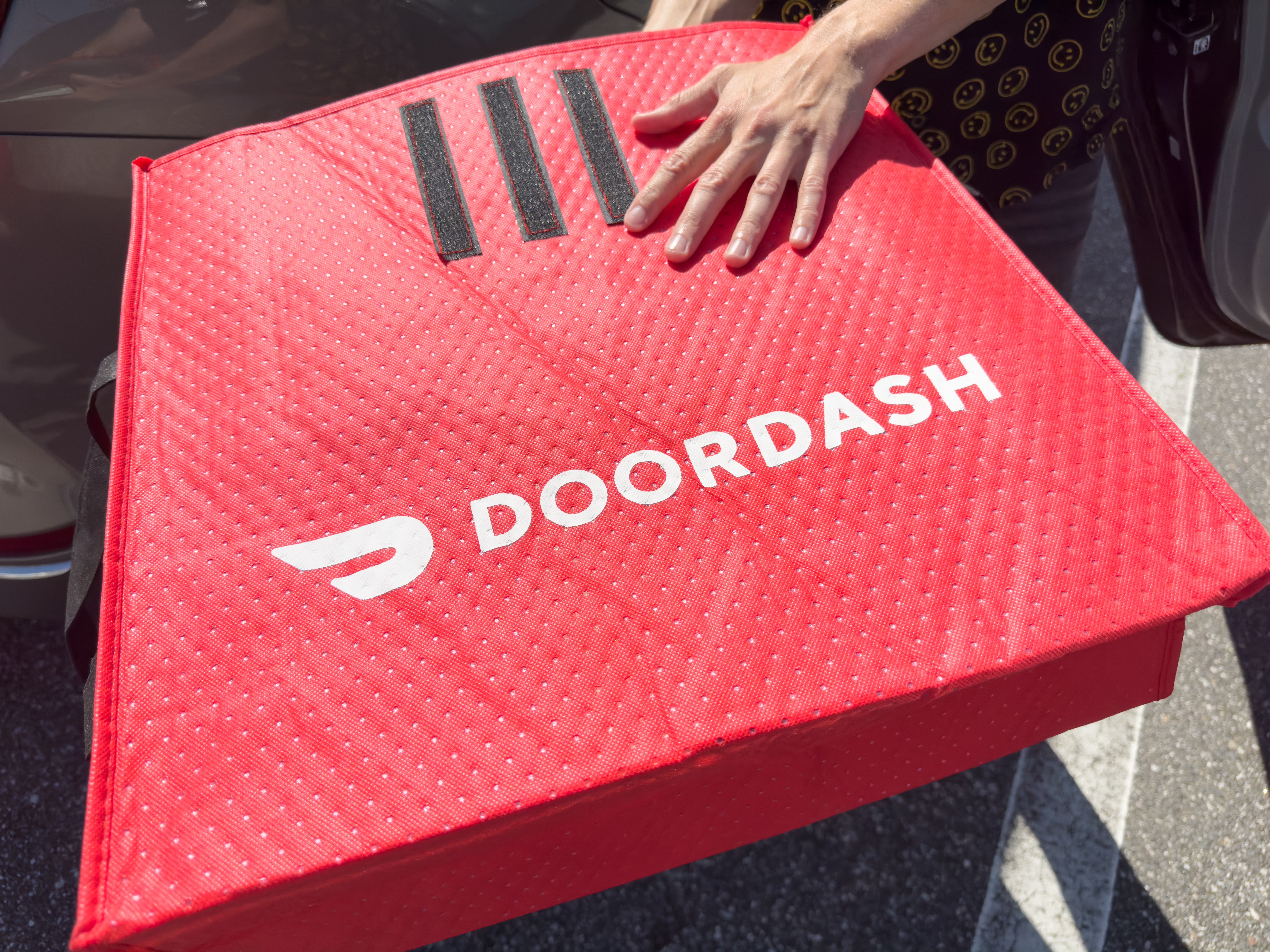 DoorDash insulated delivery bag being carried beside a vehicle during a food delivery pickup.