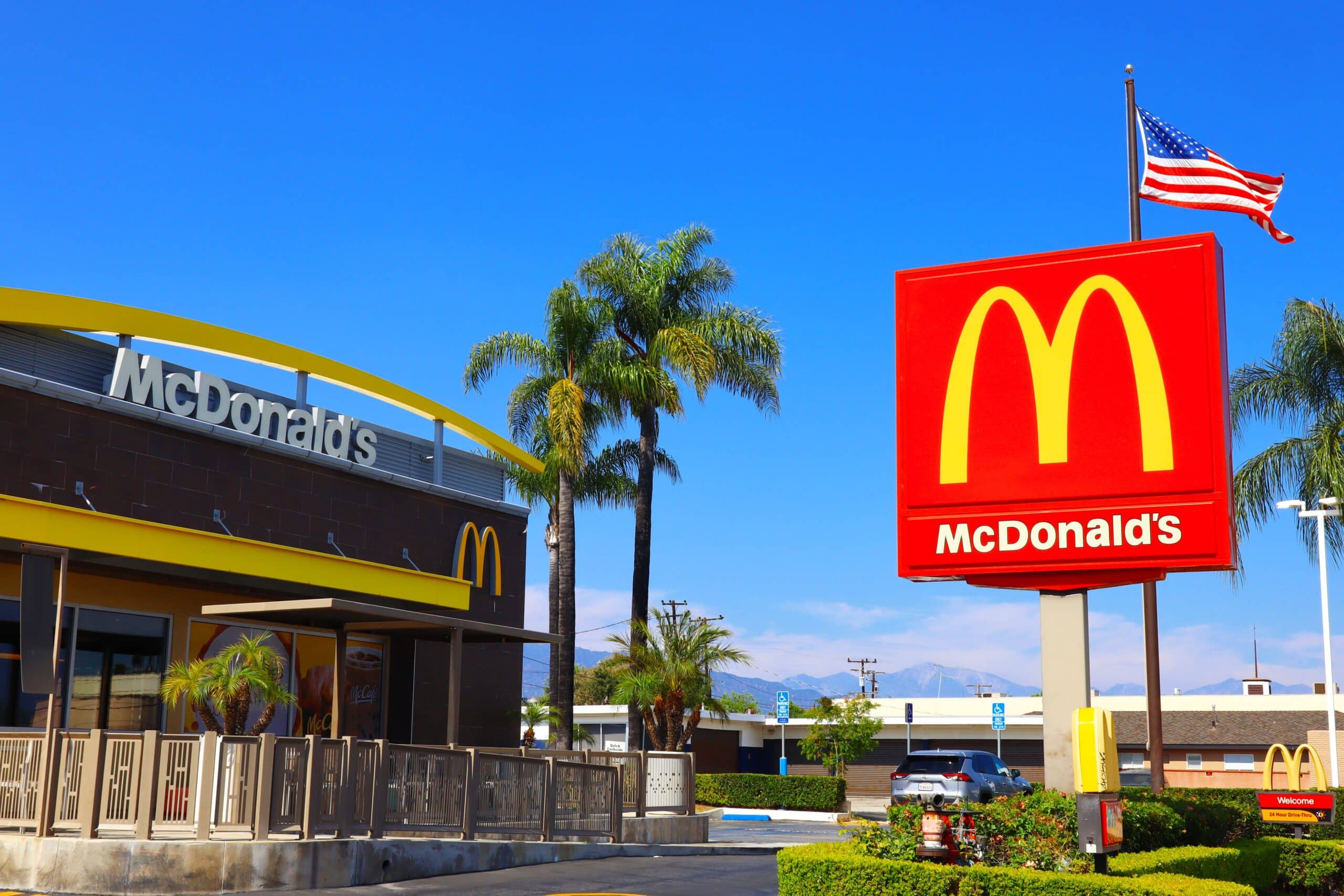 McDonald’s restaurant exterior with a large Golden Arches sign and an American flag under a clear blue sky.
