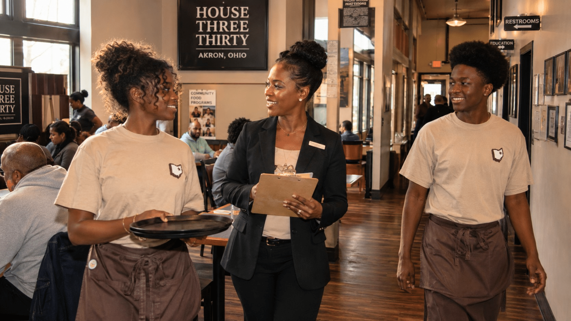 A manager holding a clipboard speaks with twins Raelyn and Raymel in the dining area of House Three Thirty in Akron.