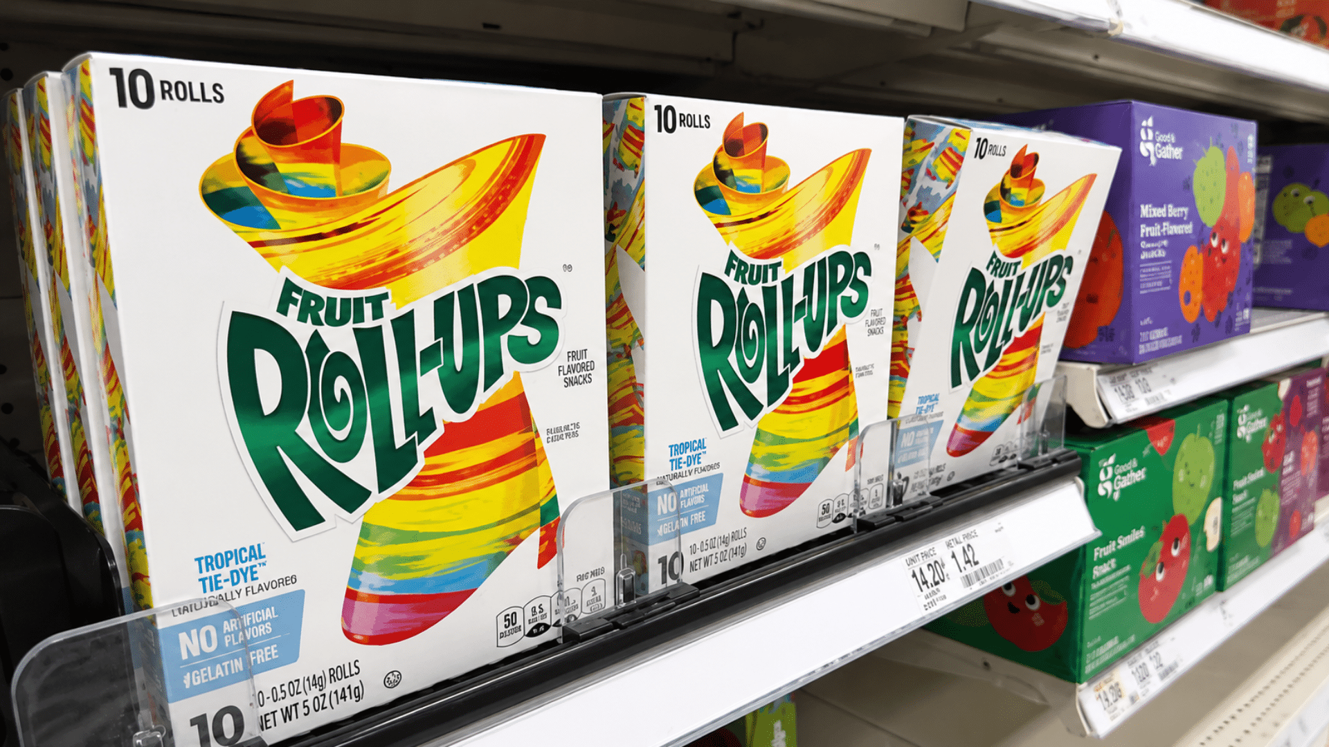 Boxes of Tropical Tie-Dye Fruit Roll-Ups lined up on a grocery store shelf with price tags visible.
