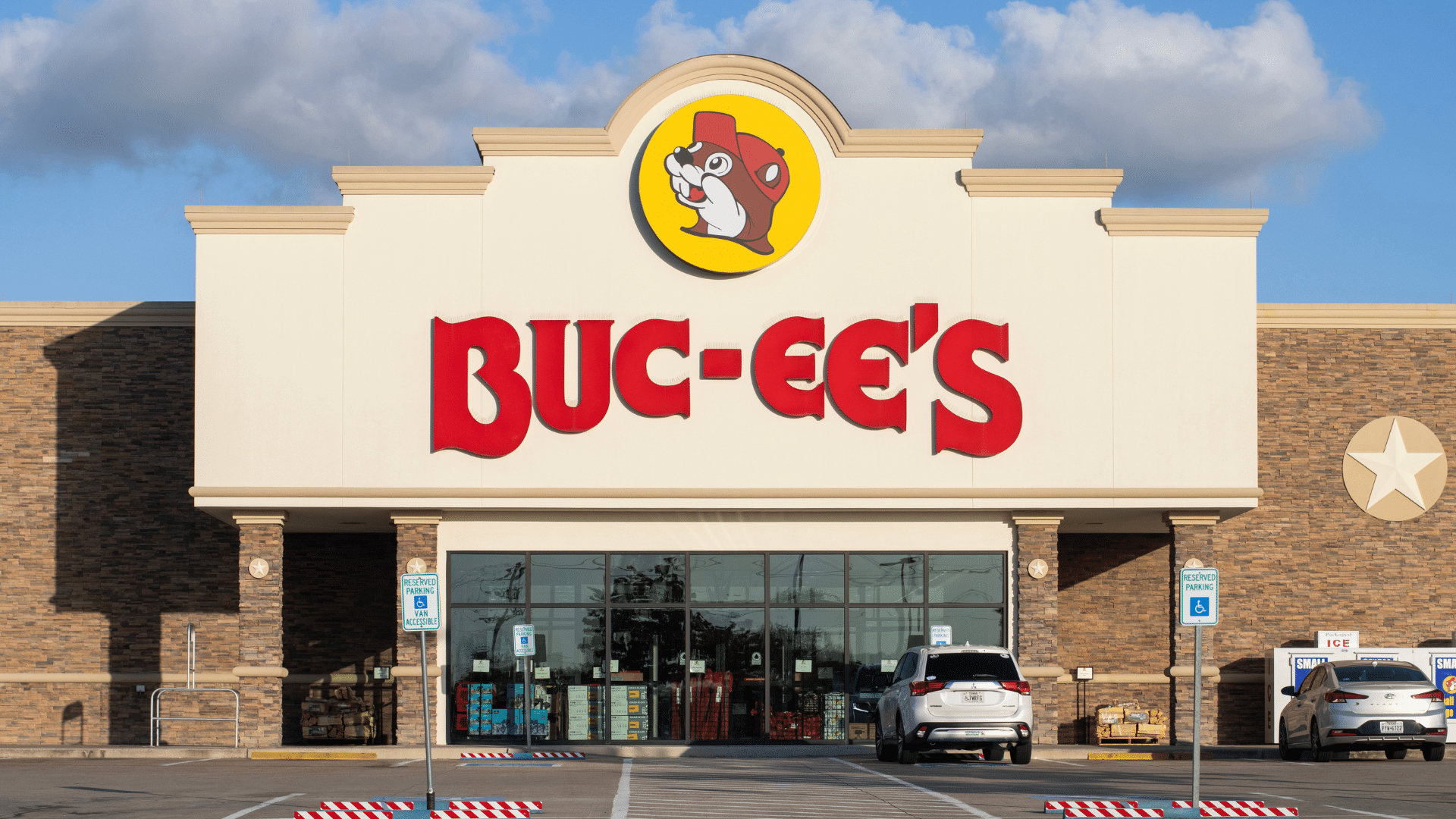 The exterior facade of a Buc-ee's convenience store featuring its large red name and beaver mascot logo on a sunny day.