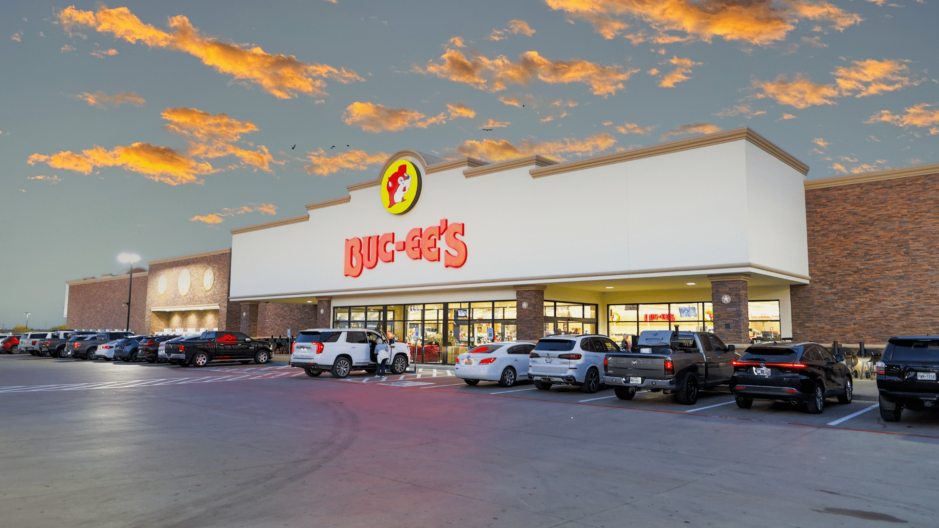 A Buc-ee's store exterior and busy parking lot viewed under a vibrant, colorful sunset sky.