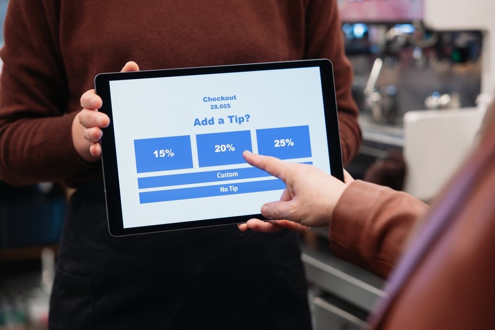 Customer selecting a tip option on a tablet payment screen held by a service worker.