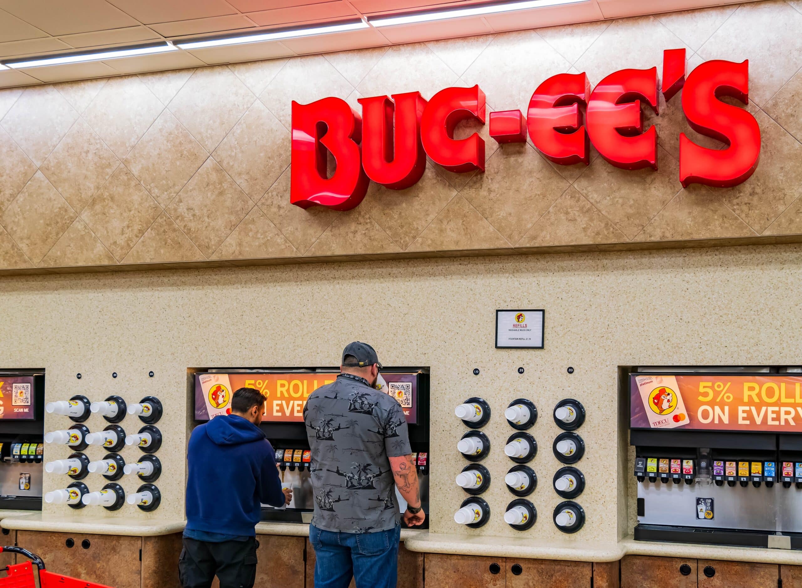 Customers fill beverage cups at a self-service drink station inside a Buc-ee's convenience store beneath the iconic Buc-ee's sign.