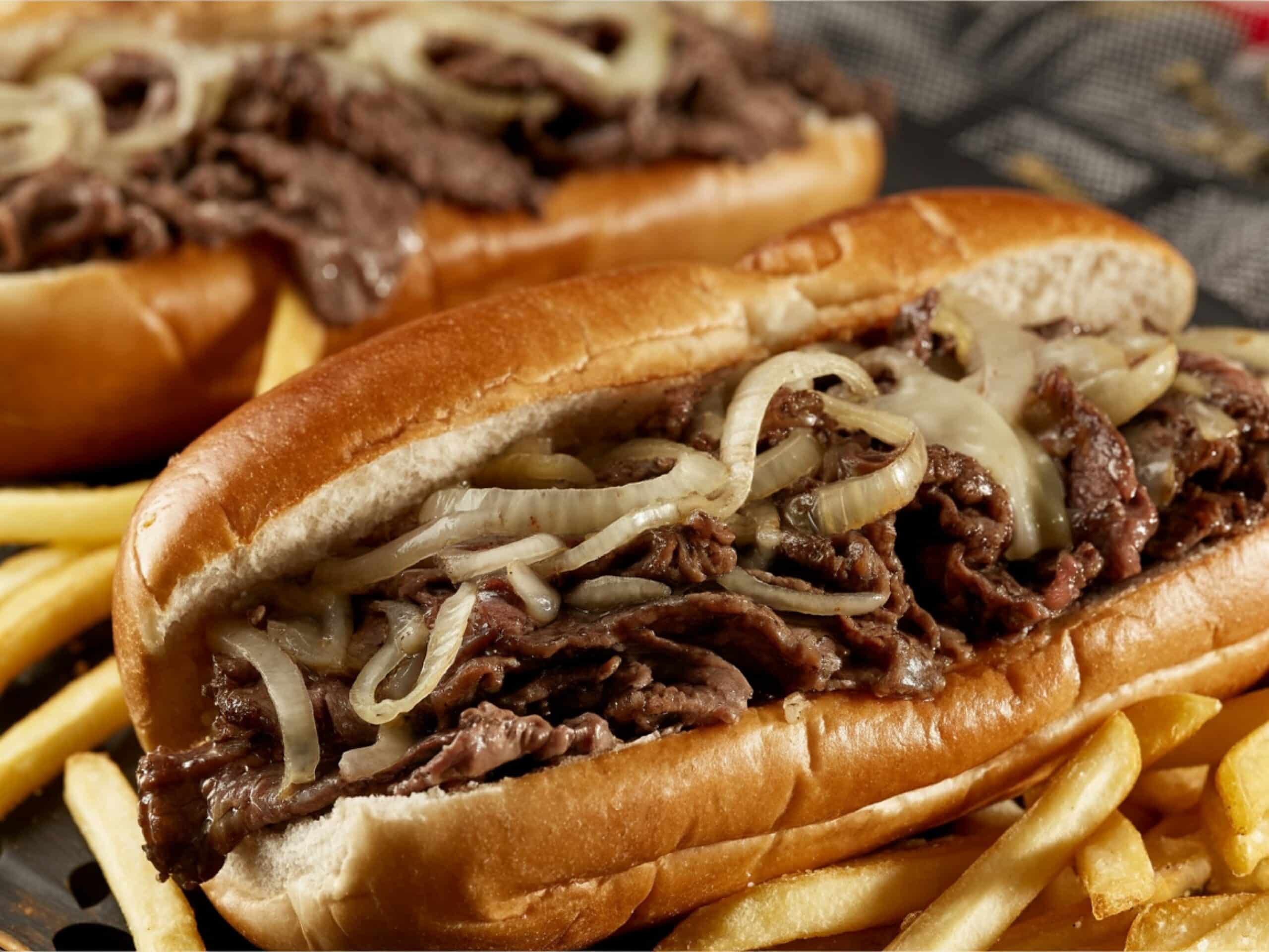Cheesesteak sandwich topped with grilled onions and melted cheese, served with French fries.