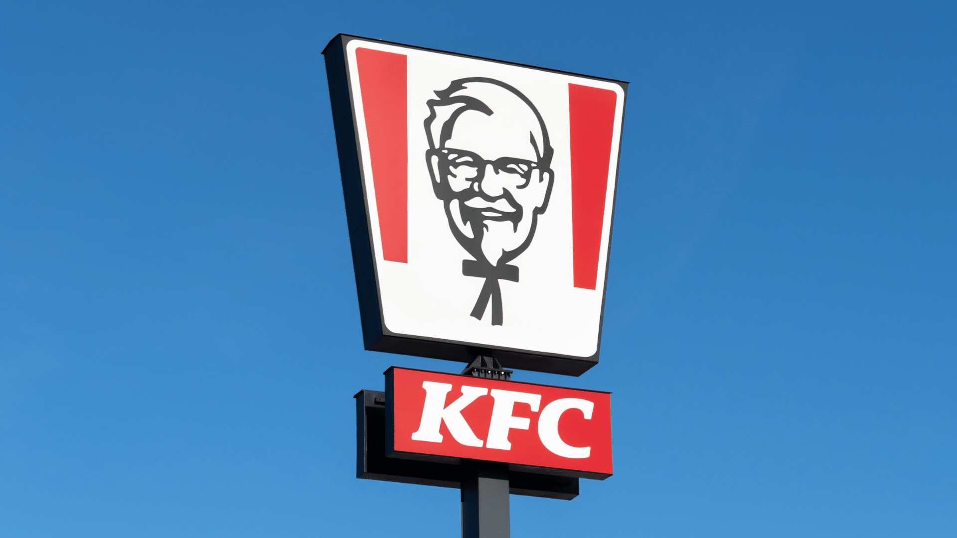 Tall outdoor KFC sign against a clear blue sky.