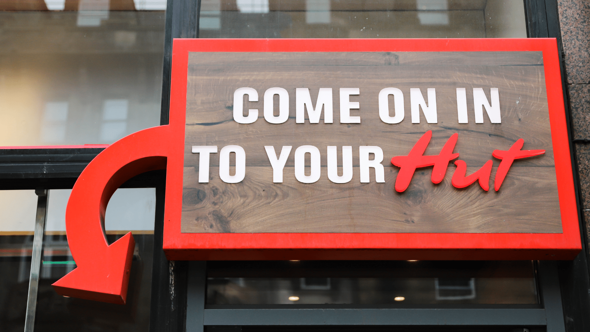 A wooden window sign with a red border and a curved arrow reads _COME ON IN TO YOUR Hut.