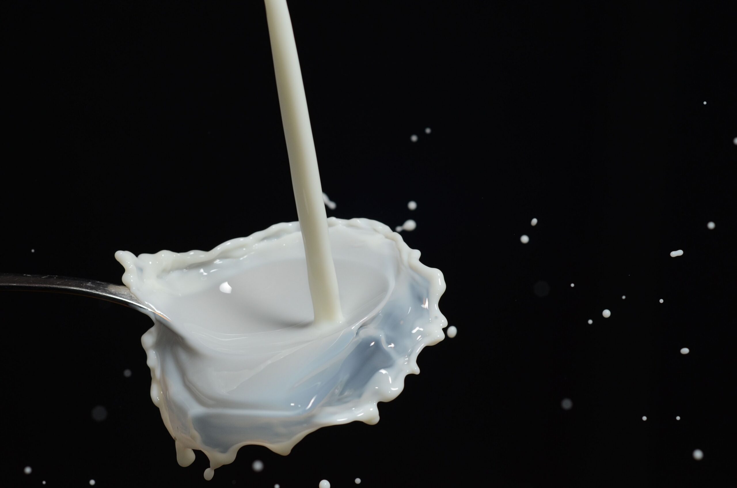 Milk splashing into a spoon against a dark background, representing the undeclared milk allergen behind the Donutful donut recall.