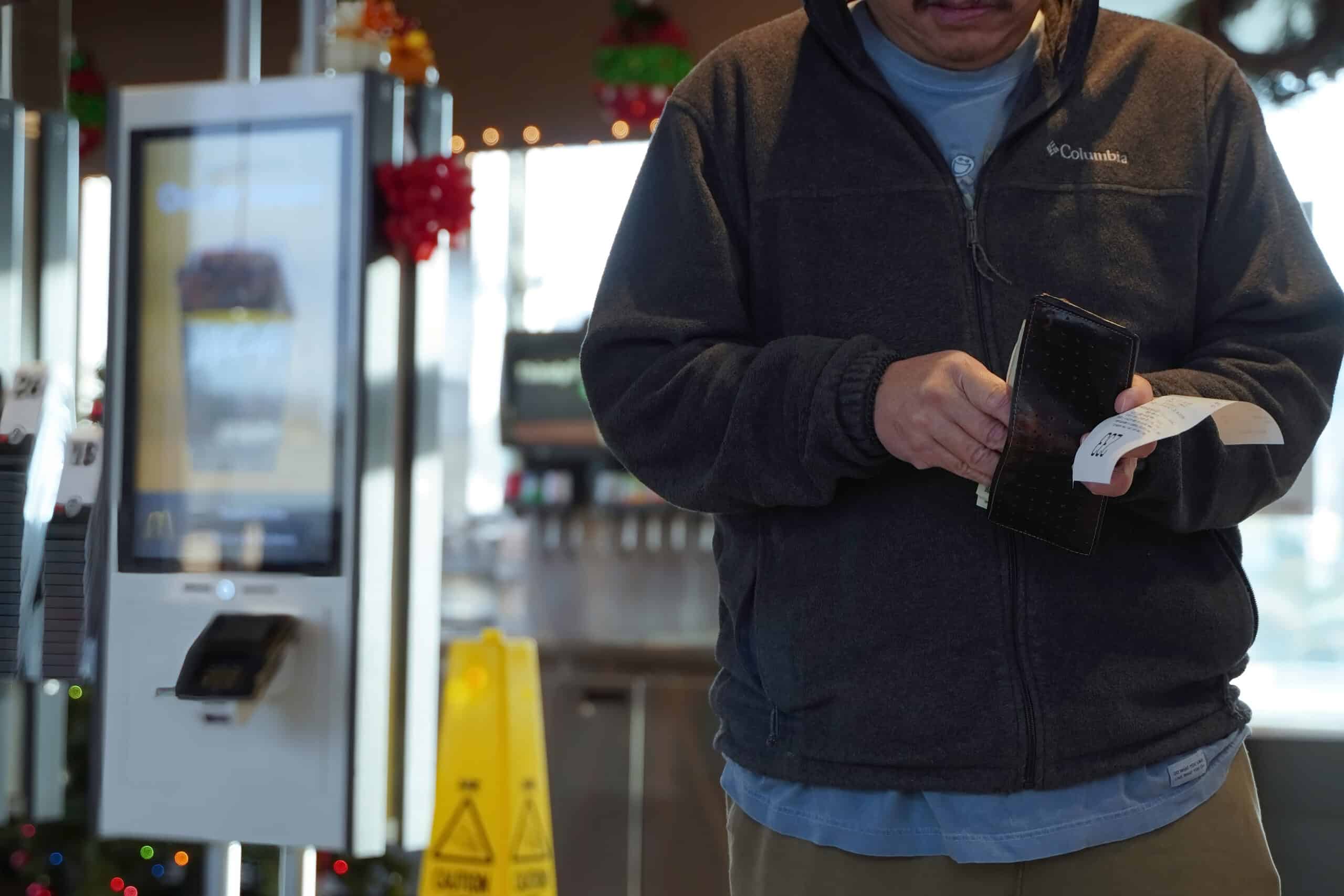 McDonald’s customer holding a receipt and wallet near a self-service ordering kiosk.