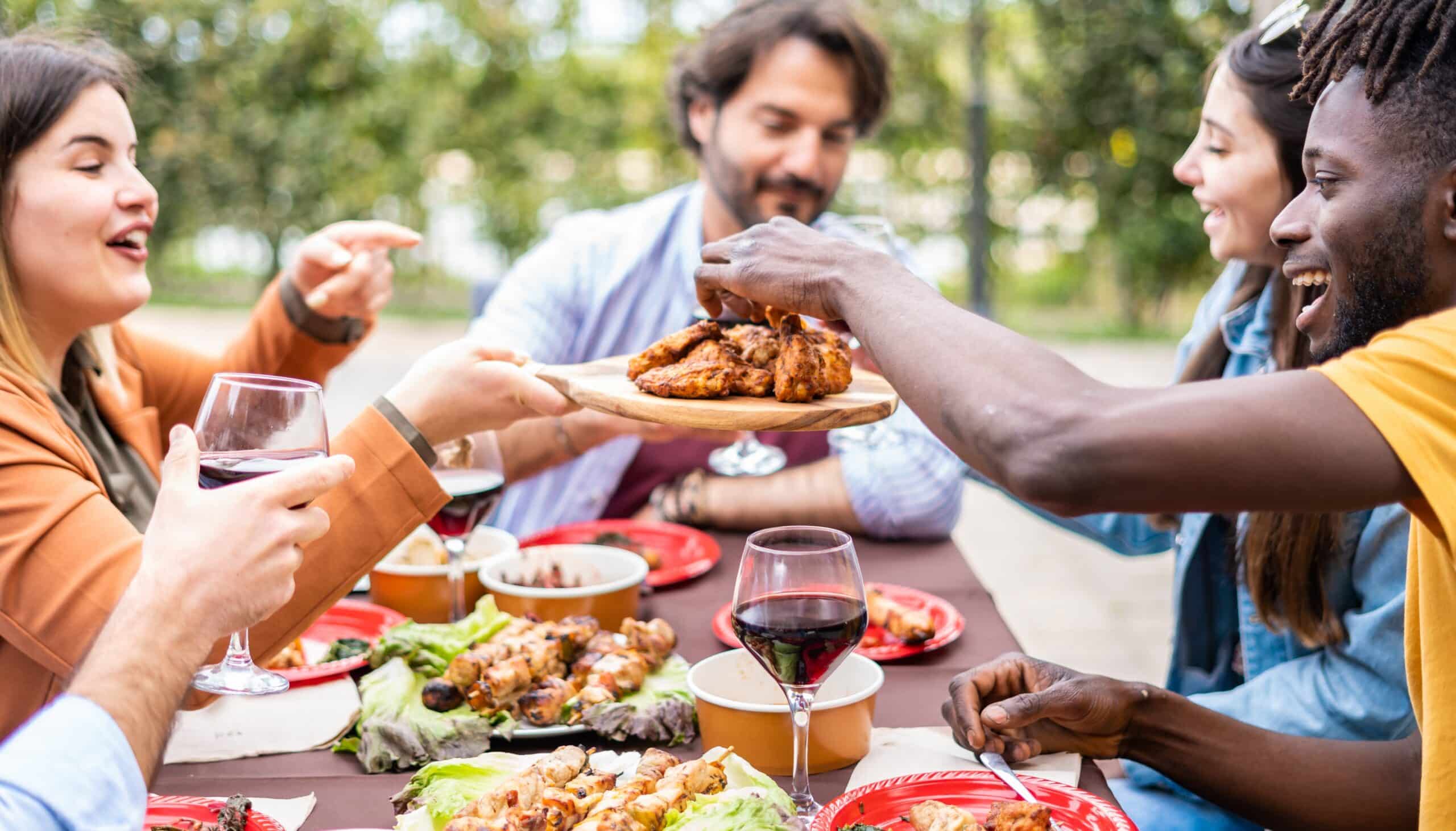 A group of friends sharing a plate of chicken wings and drinks at an outdoor gathering.