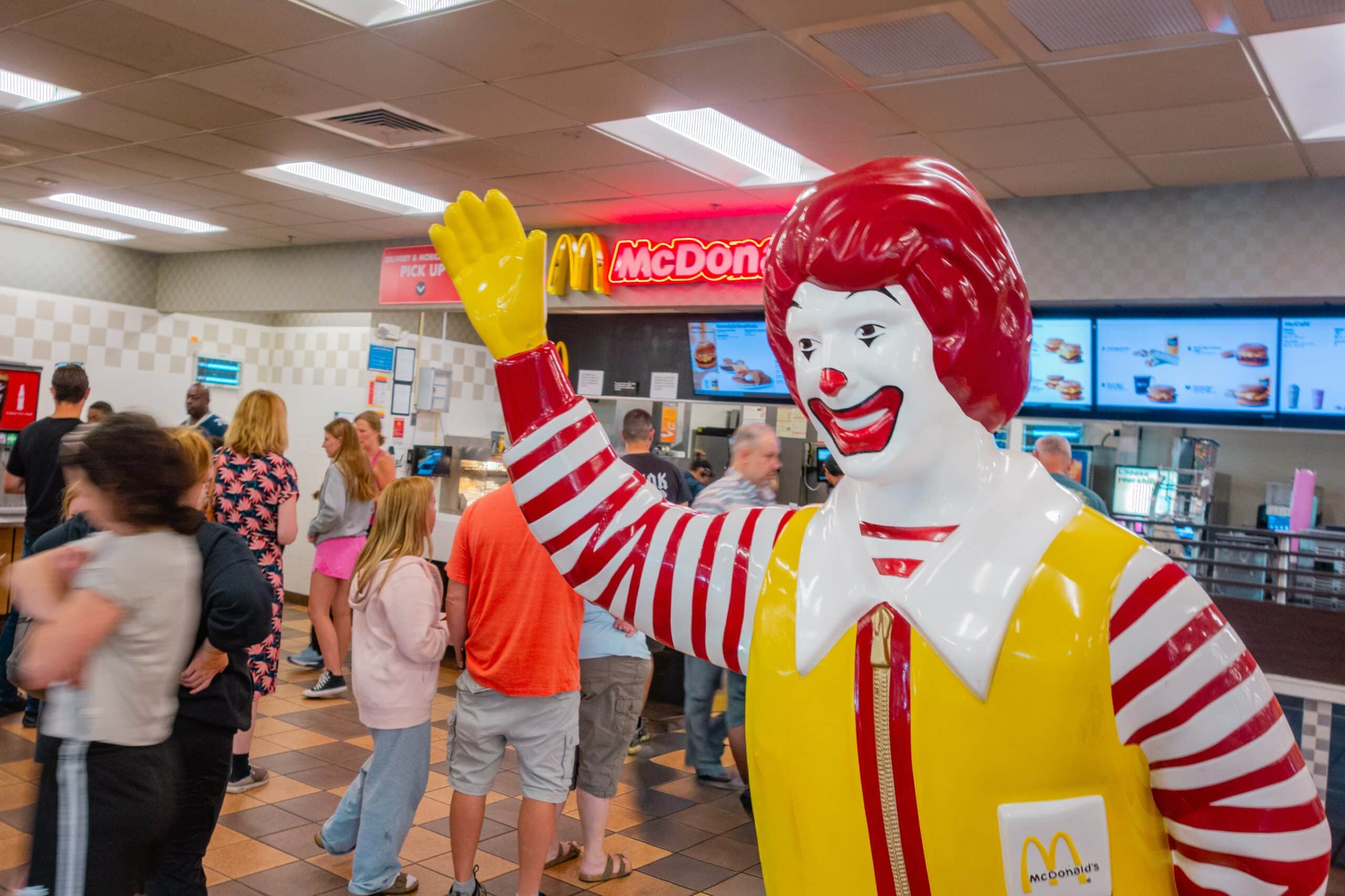 Customers inside a McDonald’s restaurant near the counter with a Ronald McDonald statue in the foreground.