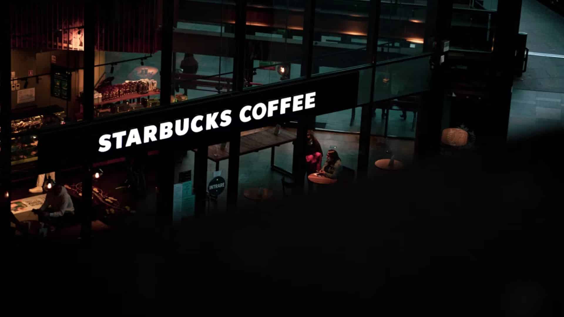 Starbucks Coffee storefront illuminated at night with customers visible inside.