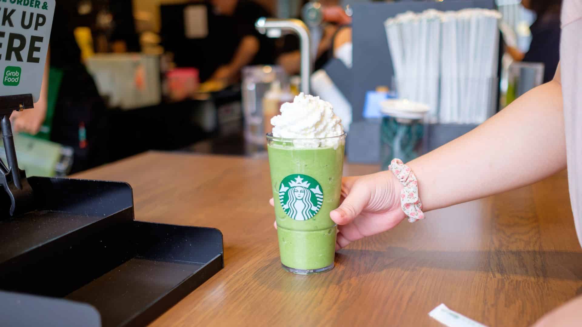 Customer picking up a green Starbucks blended drink topped with whipped cream.