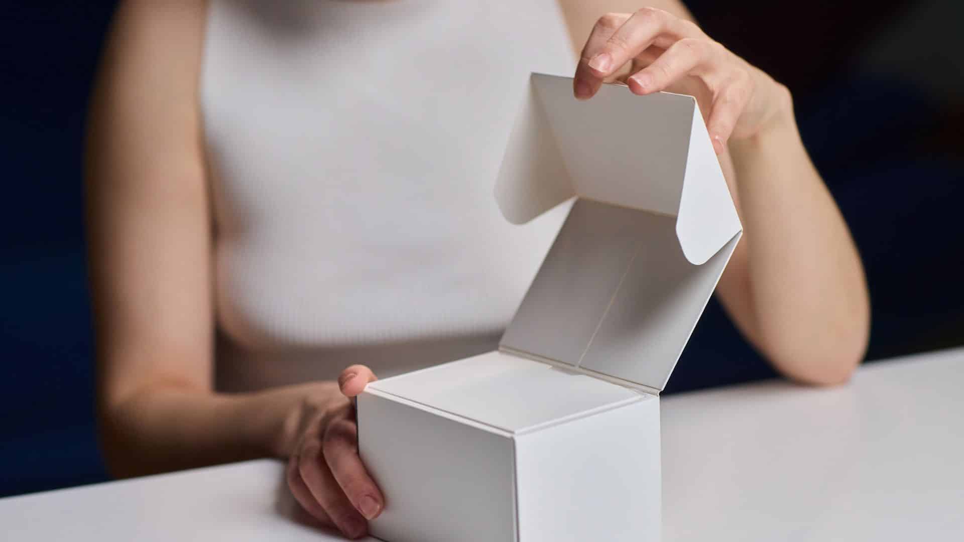 Person opening an empty white cardboard takeout box on a table.