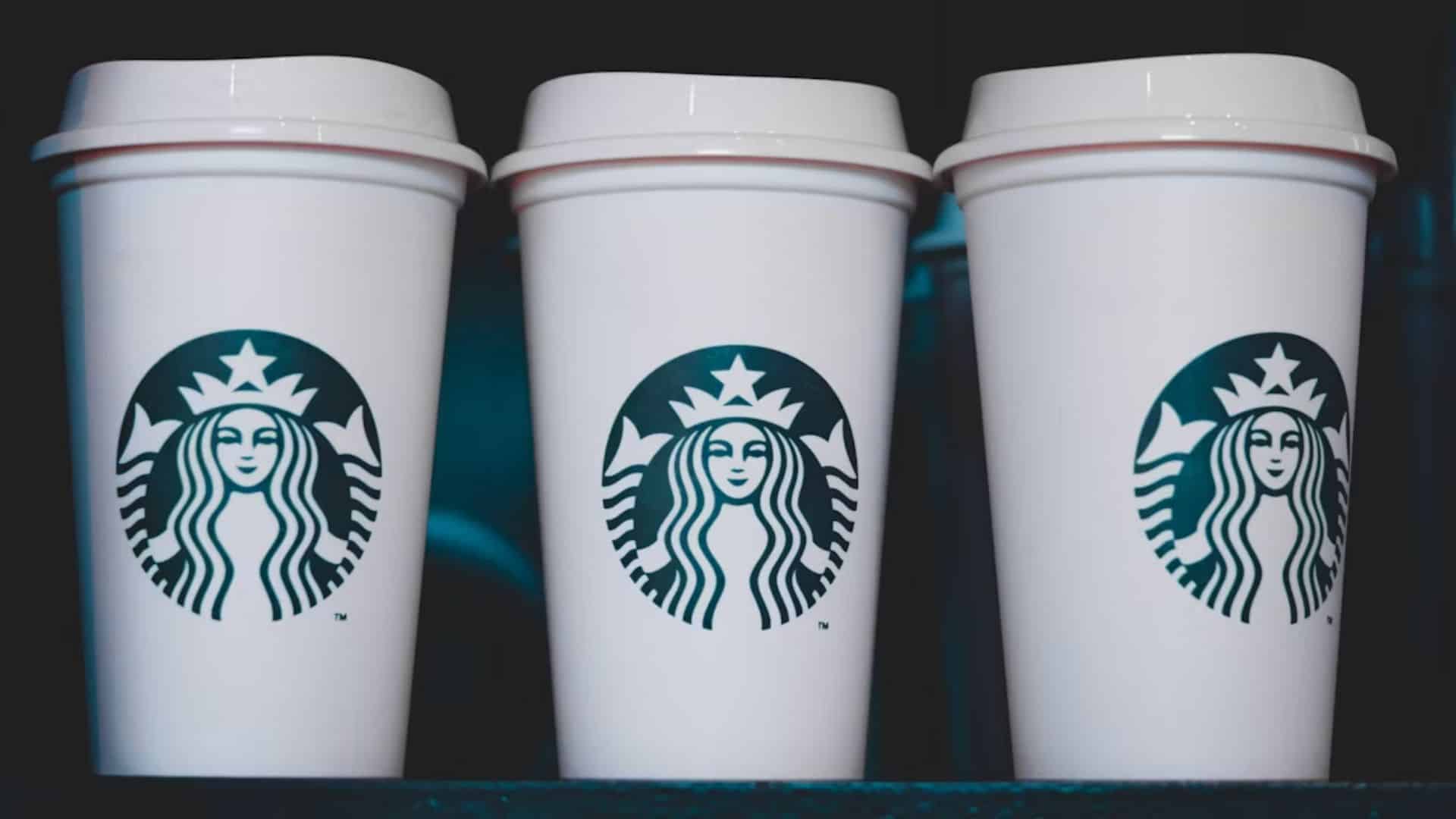 Three white Starbucks takeaway coffee cups with green siren logos.