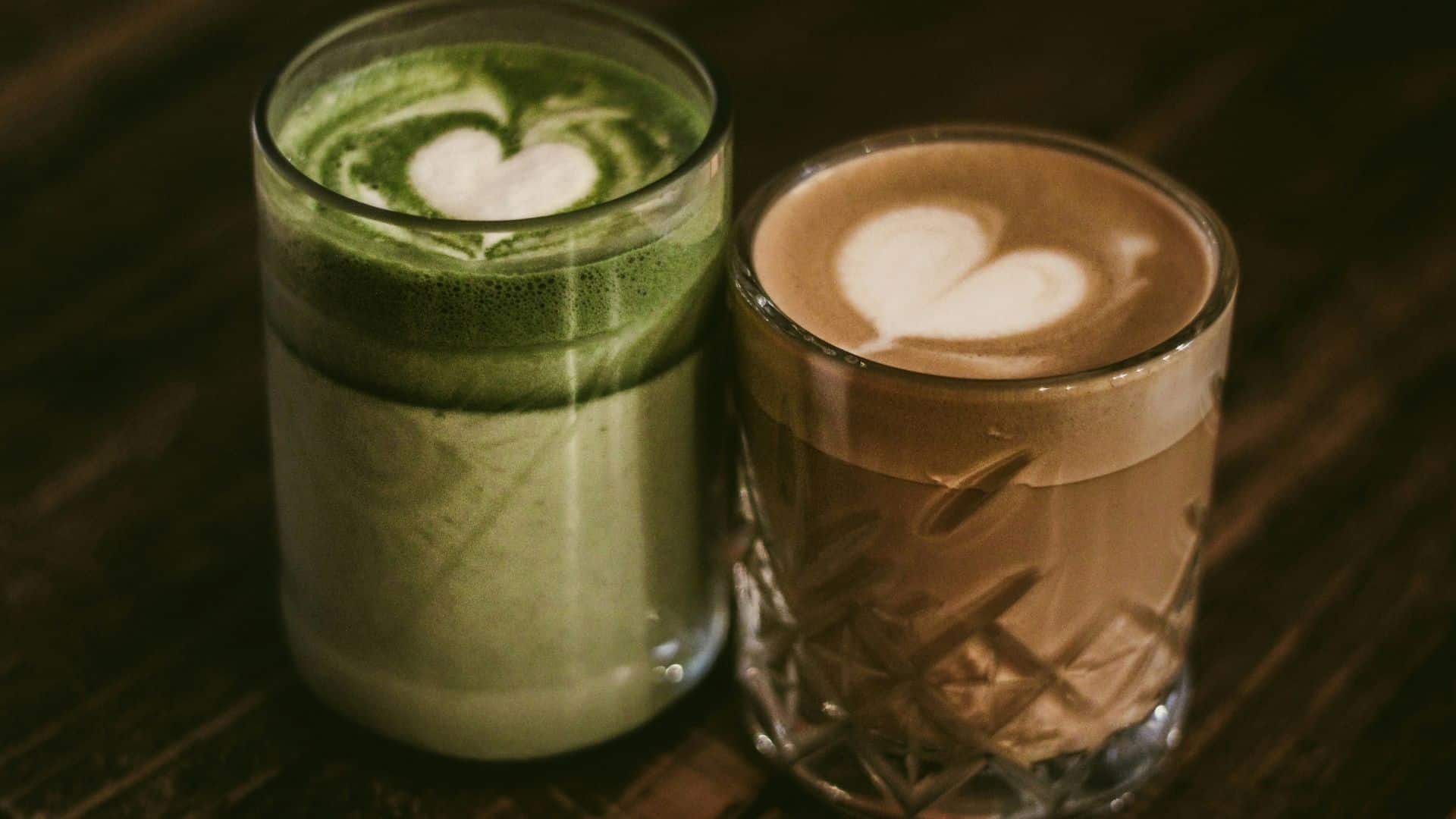 Green matcha drink and coffee served with heart-shaped foam art.