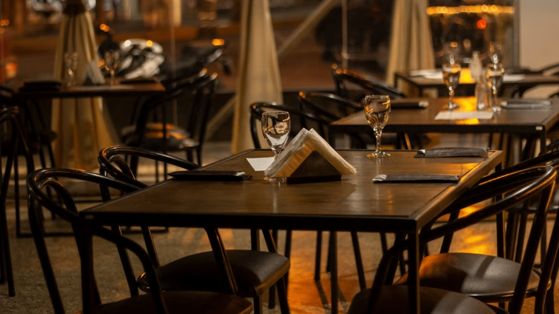 Empty tables set with glasses and napkins at an outdoor restaurant at night.