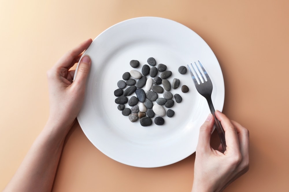 Hands holding a plate filled with small stones alongside a fork, illustrating the risk of foreign objects in food.