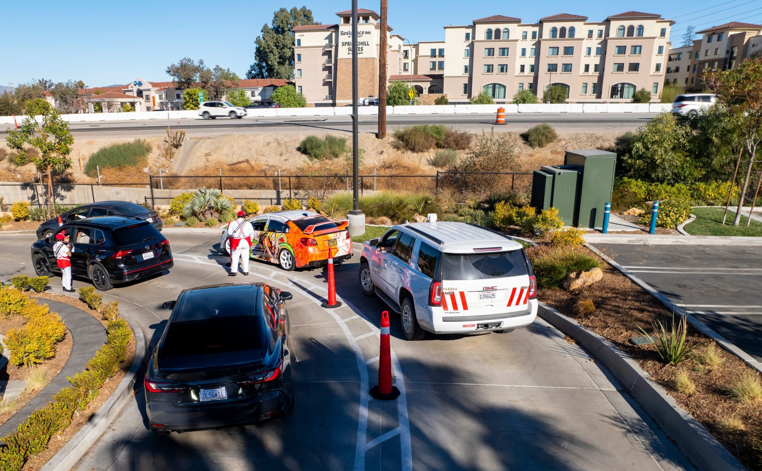 Cars line up in an In-N-Out drive-thru as employees direct vehicles through the busy lane.