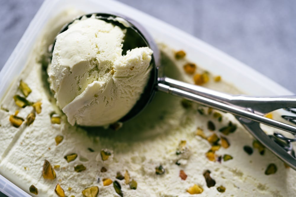 A scoop of a frozen dessert lifted from a container topped with chopped nuts.