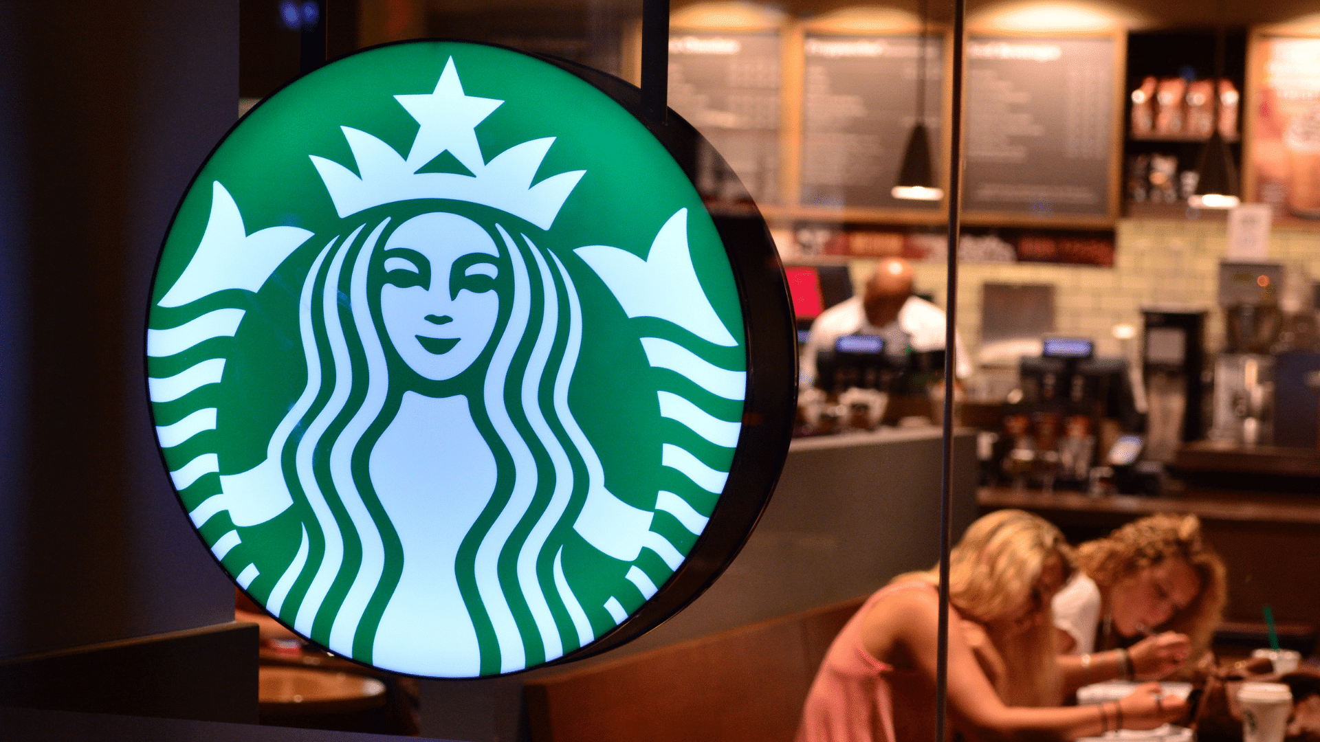 Illuminated Starbucks circular logo mounted in a cafe window.