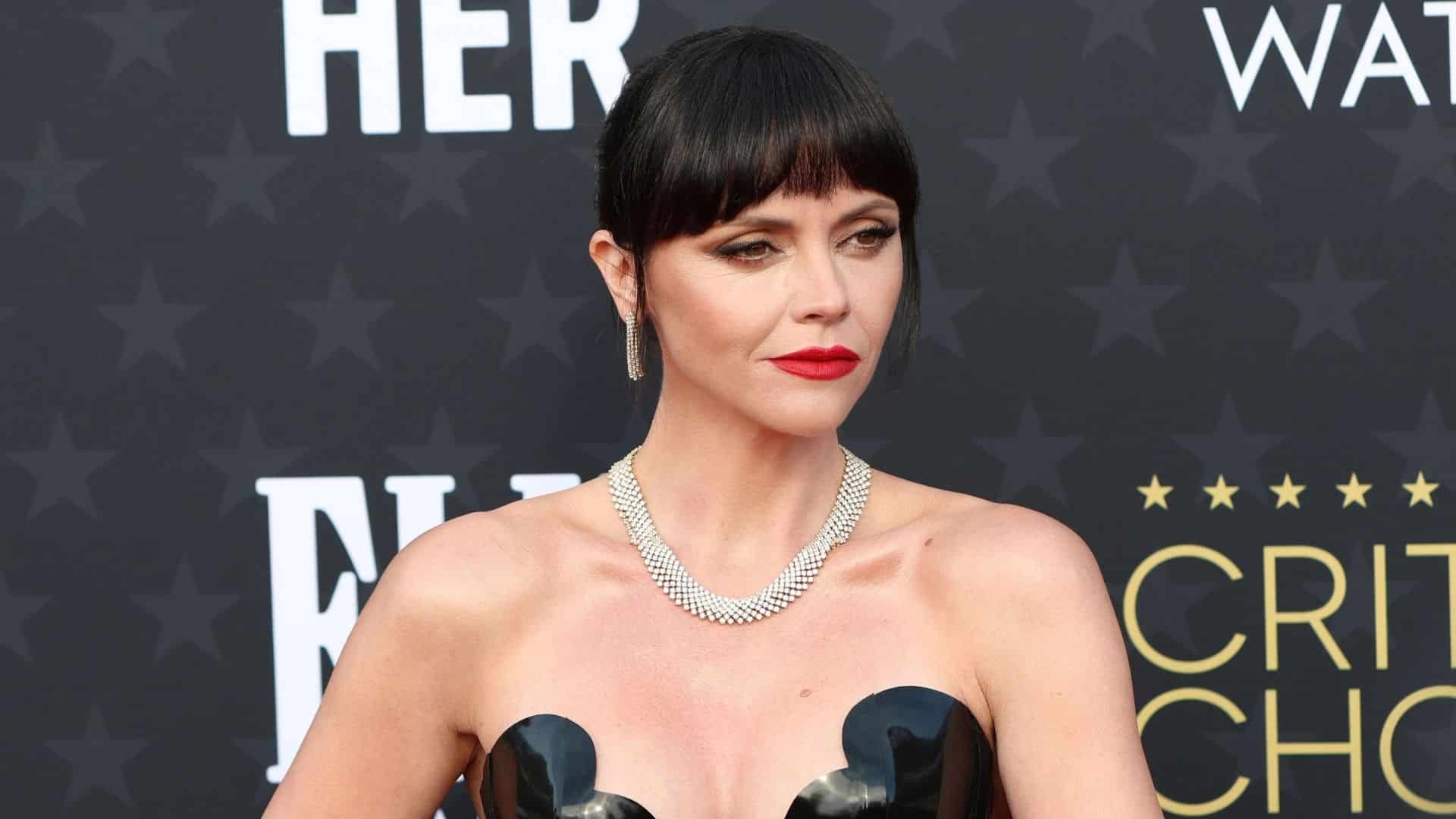 Christina Ricci with dark bangs and red lipstick wearing a black strapless gown and diamond necklace at the Critics Choice Awards.