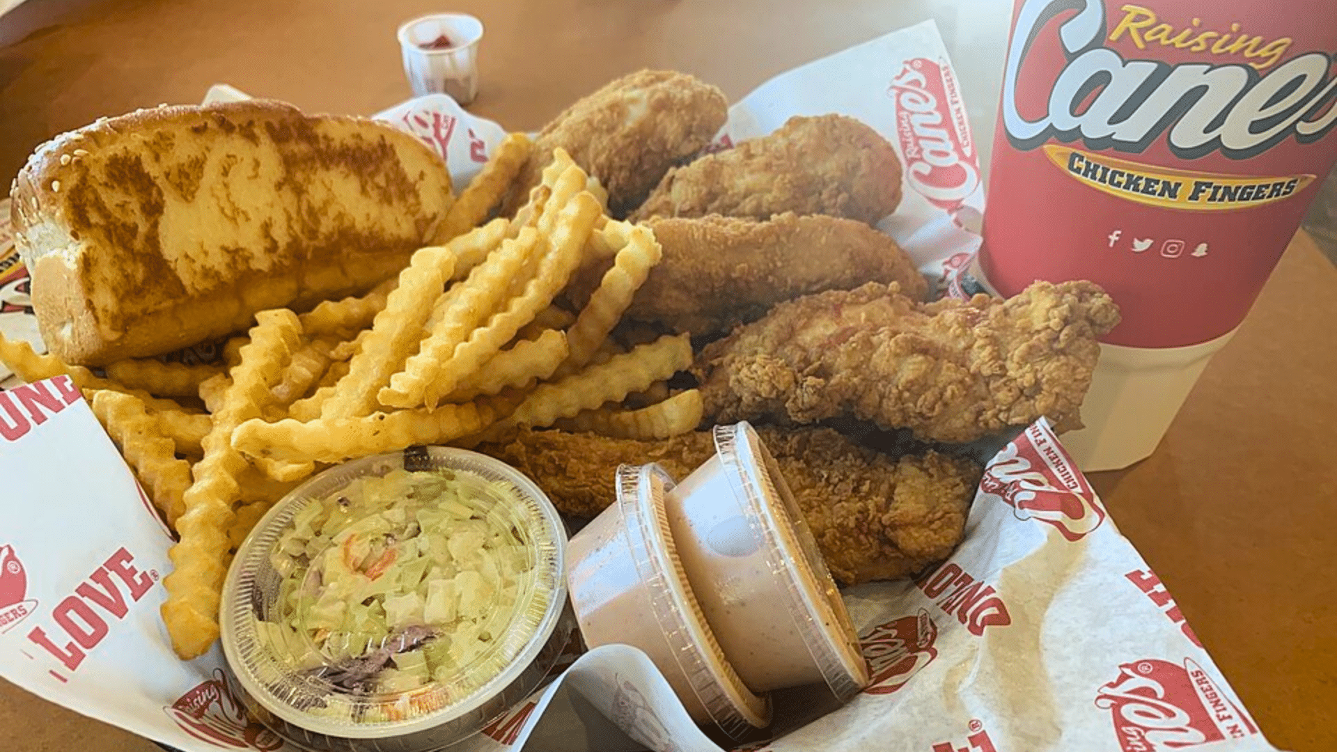A basket of Raising Cane's chicken fingers, fries, toast, and coleslaw.