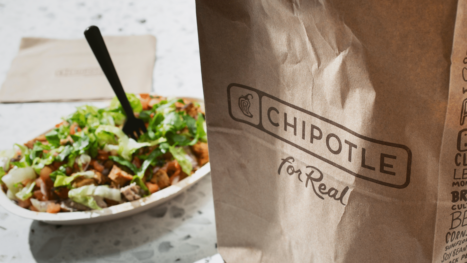 Chipotle paper takeout bag next to a Chipotle bowl.