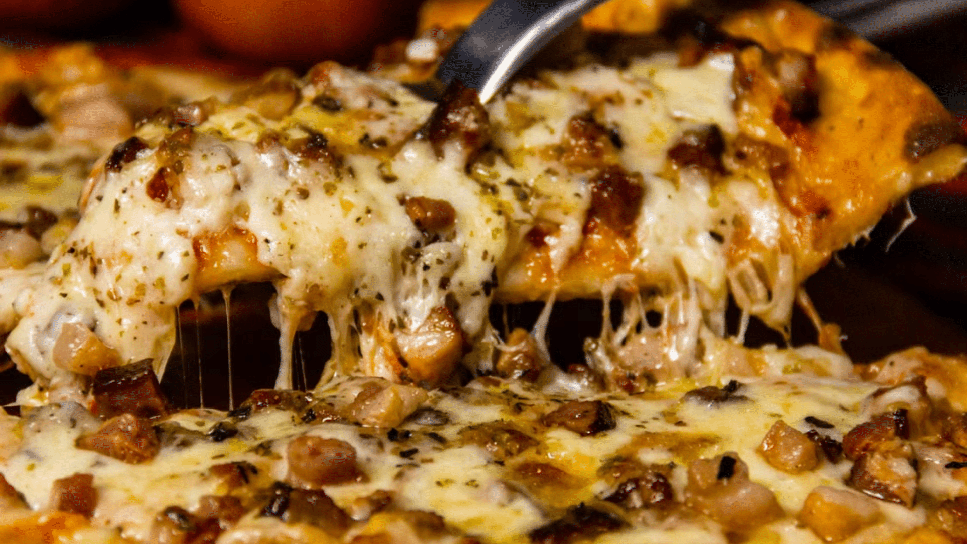 A slice of pizza topped with melted cheese and seasoned meat and beans is lifted with a spatula.