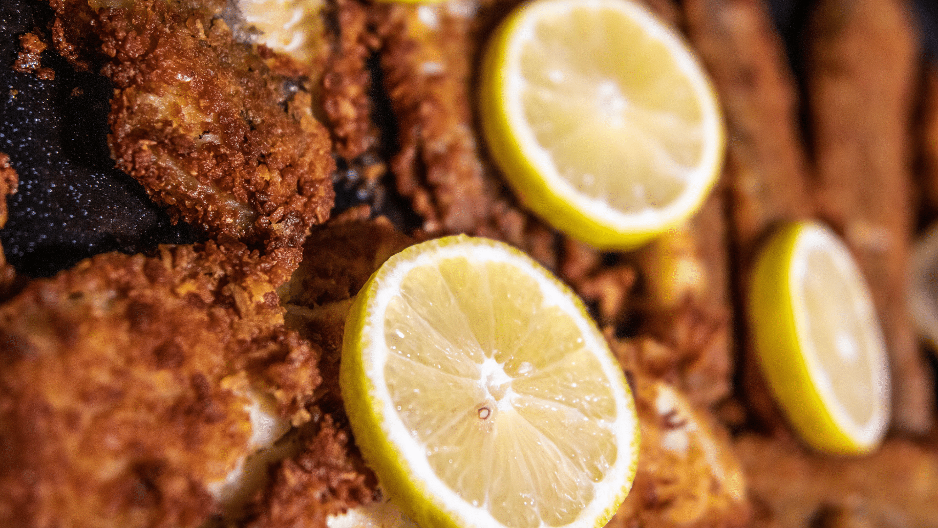 Freshly fried fish fillets are served with bright yellow lemon slices laid across the top.