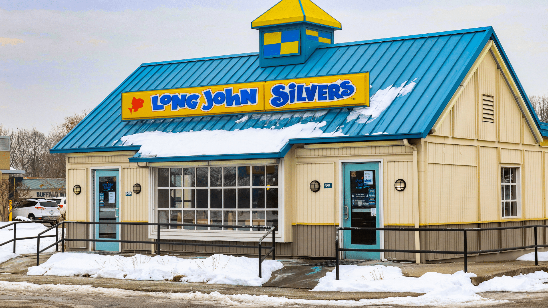 The exterior of a standalone Long John Silver's fast-food restaurant with a bright blue metal roof in a snowy setting.