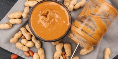 Bowl with delicious peanut butter, empty jar and nuts on table